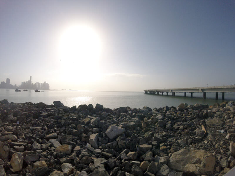 Rocky shoreline with a distant pier and hazy skyline silhouette near Panama City at sunset