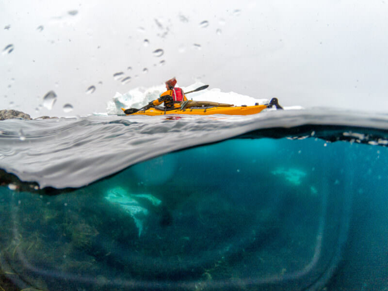 Over/under dome port shot of a kayaker by icebergs, water droplets from a leak visible on the dome