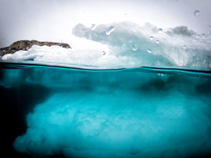 Over-under dome shot of a floating iceberg's jagged white edge meeting turquoise Arctic water