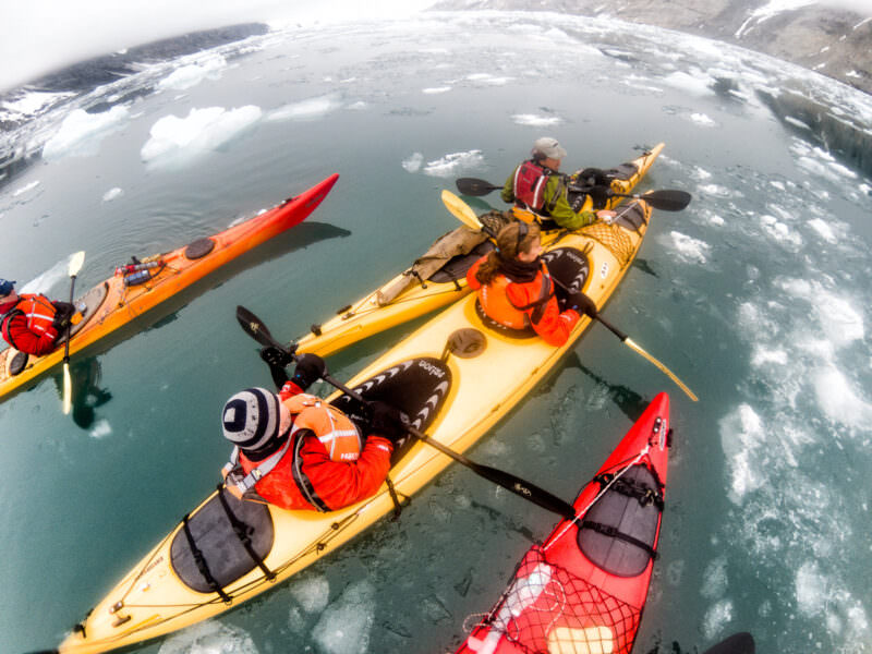 Overhead fisheye view of sea kayakers paddling through icy arctic waters in Svalbard