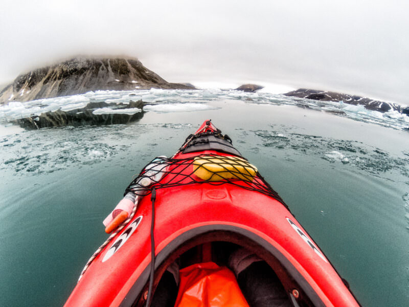 Red kayak's bow gliding through icy waters near snow-dusted cliffs in Svalbard