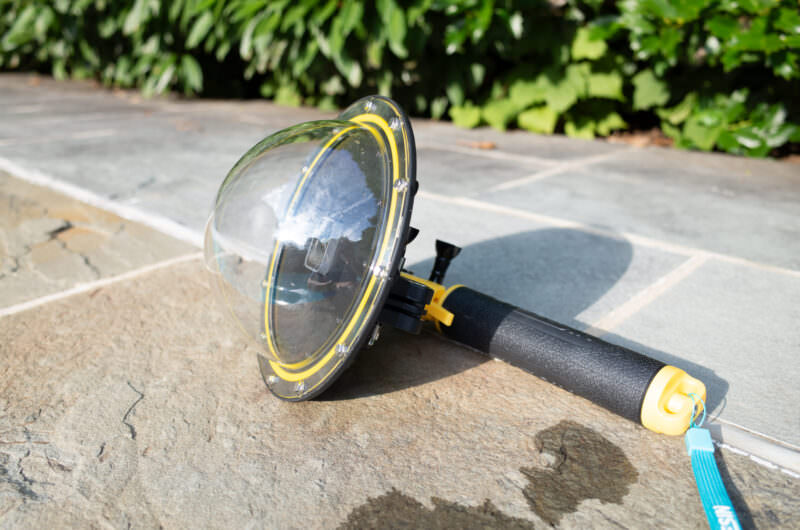 Fully assembled GoPro dome port with pistol-grip handle resting on a stone surface