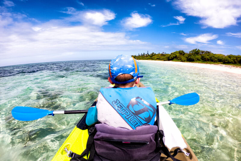 Boy in a kayak paddling toward a sandy island through shallow turquoise water