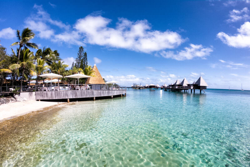 Overwater bungalows and thatched huts along a turquoise lagoon in New Caledonia
