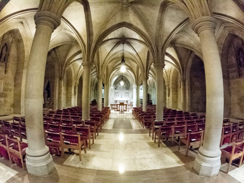 Empty stone chapel with vaulted arches and rows of wooden pews leading to an altar