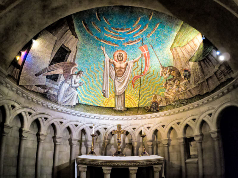 Byzantine-style mosaic of a resurrected Christ above the altar in a dimly lit chapel
