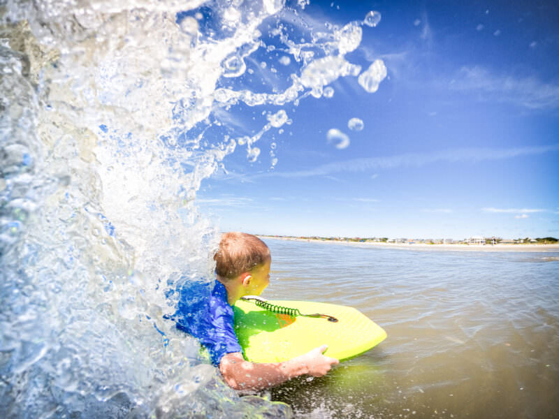 Boy on a yellow bodyboard caught in a splashing wave along a sandy shoreline