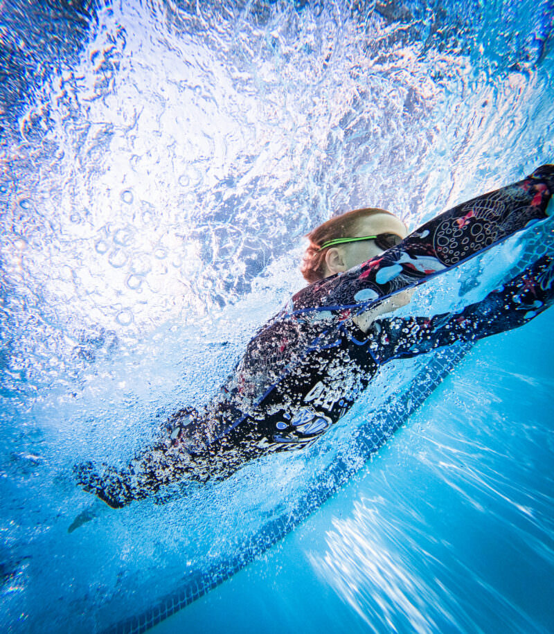 Girl in a patterned swimsuit gliding underwater in a sunlit pool