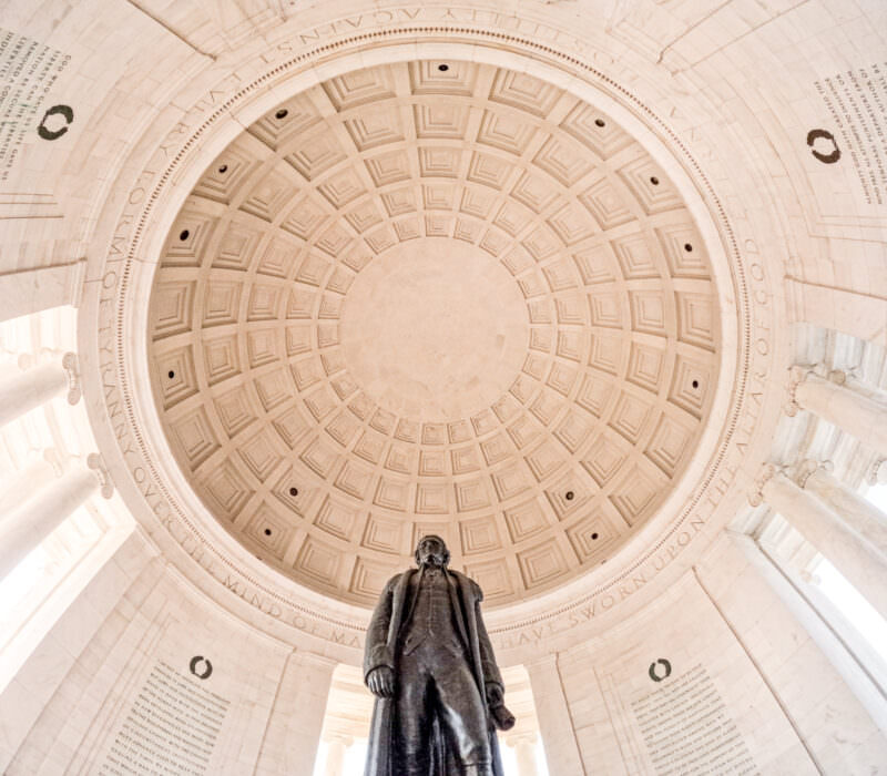 Bronze statue of Thomas Jefferson standing beneath the coffered dome of his memorial in Washington DC