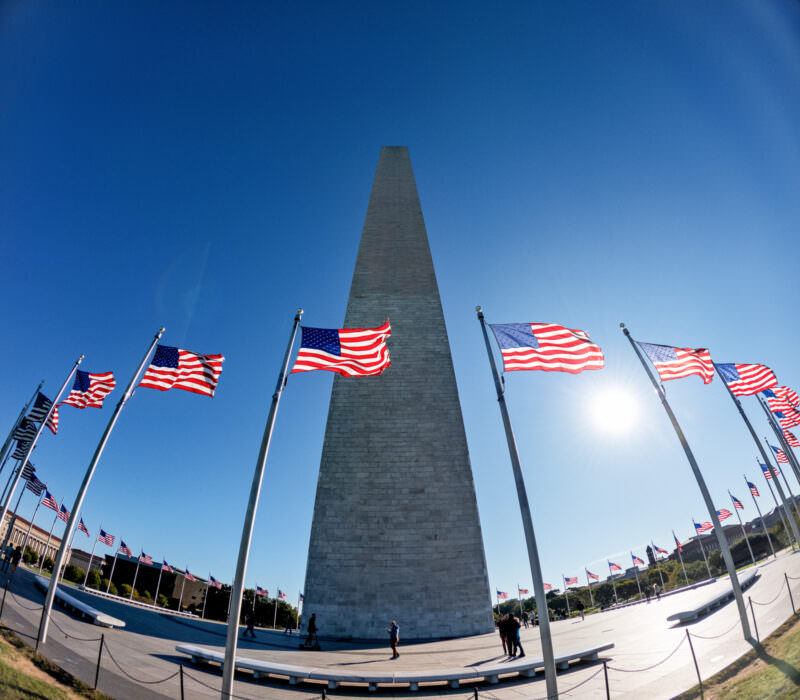 Washington Monument framed by ringed American flags under a bright blue sky