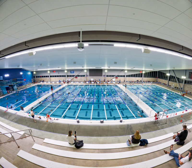 Indoor competition pool viewed from bleacher seating with swimmers in the lanes