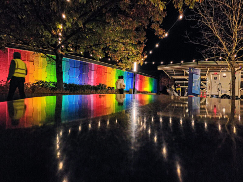 Night sample shot from the Insta360 Ace Pro 2 of a rainbow-lit memorial wall reflected on wet pavement