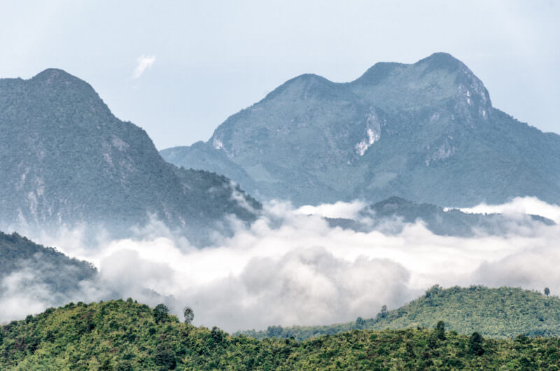 Forested limestone karst peaks rising through valley fog, steep vertical rock faces with layered vegetation