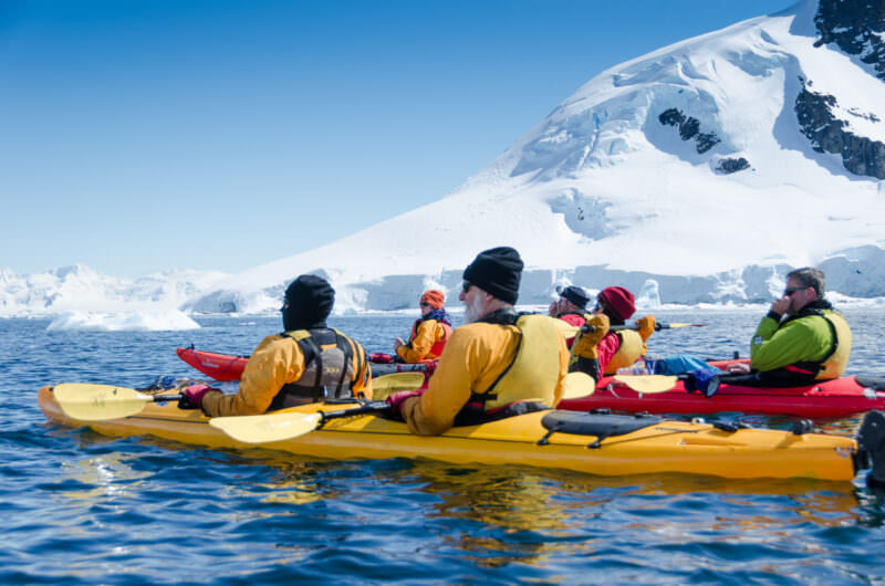 Expedition kayakers rafted together on Errera Channel with glaciated mountains behind, Cuverville Island