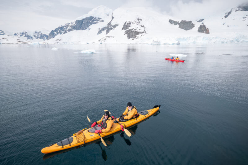 Aerial view of tandem kayakers navigating calm waters surrounding Cuverville Island, Errera Channel