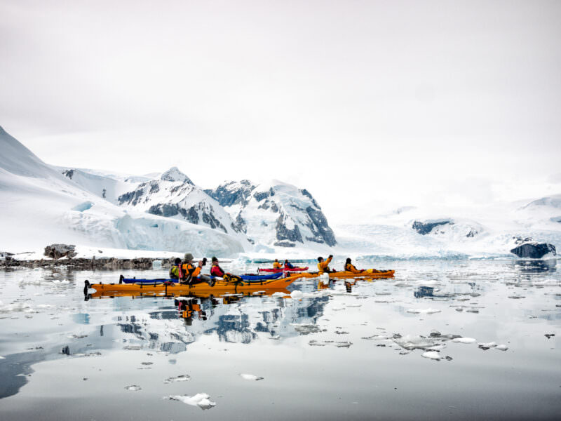 Group of kayakers navigating glassy waters with brash ice at Cuverville Island, Errera Channel