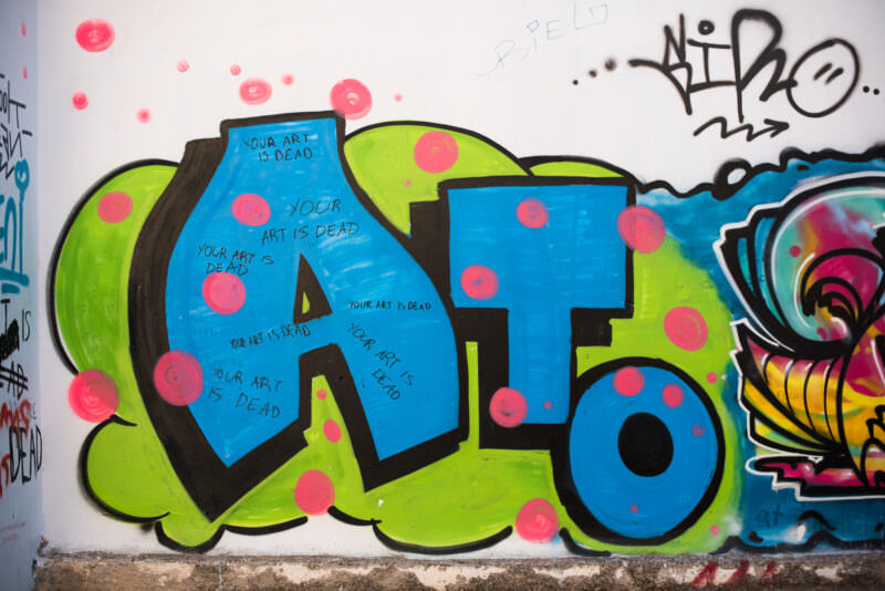 Athens street art on a wall reading "YOUR ART IS DEAD" in blue block letters on green and pink bubble shapes with polka dots
