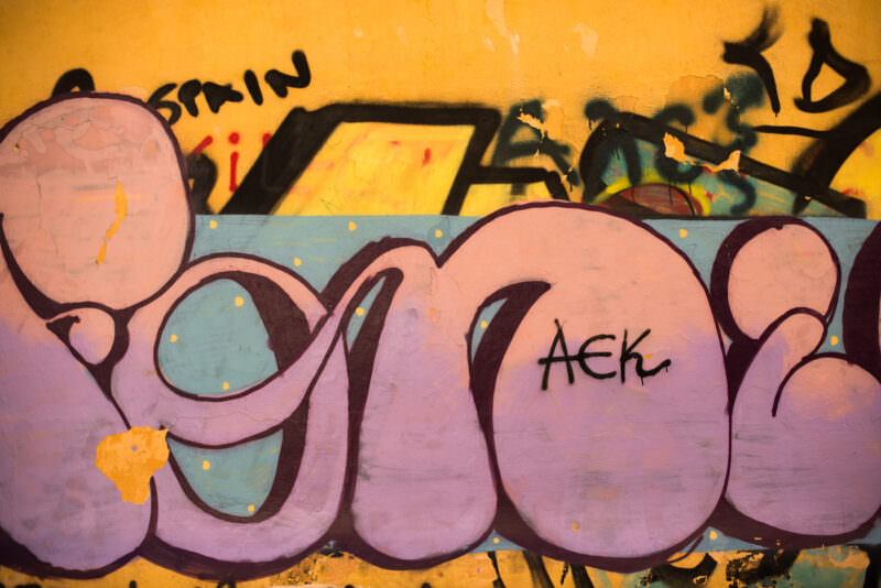 Athens graffiti on a golden-yellow wall showing bubble-letter style in pink and blue tones with abstract rounded shapes
