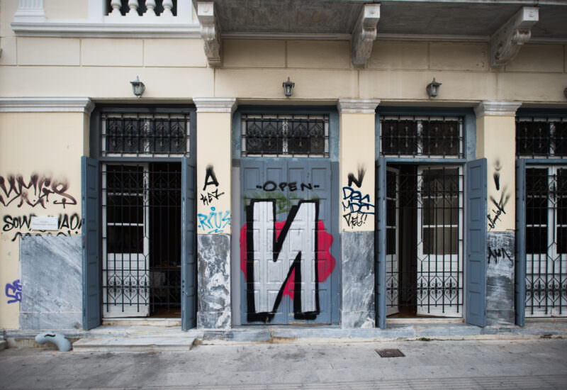 Athens street art on a neoclassical building facade showing graffiti tags and a large letter "M" painted in black, white, and red