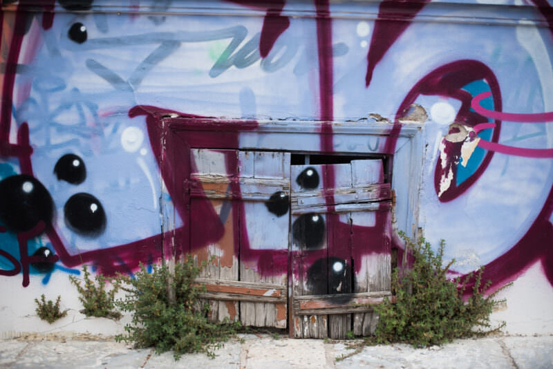 Athens graffiti detail on a weathered doorway showing abstract shapes, black drips, and colorful tags layered over peeling paint