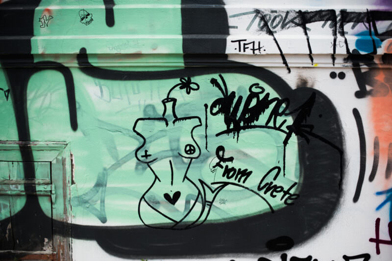 Athens graffiti detail on a mint-green wall showing a female torso outline in black with spray-painted tags and a black oval frame