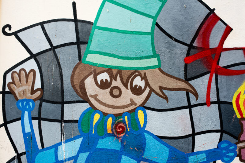 Athens street art detail showing a smiling cartoon child in a turquoise hat against a stained-glass-style mosaic background