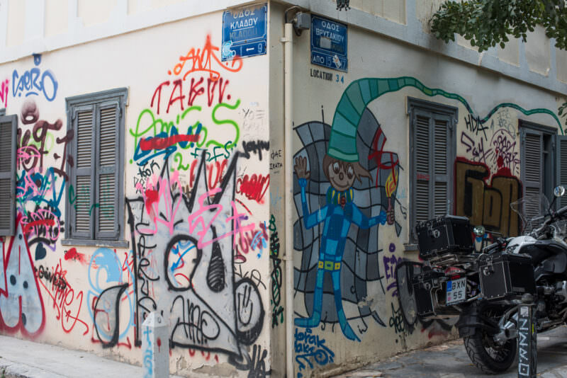 Athens graffiti on a corner building featuring a blue-suited astronaut figure beside layered colorful tags in pink, orange, and green