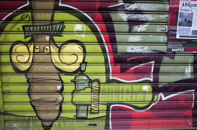 Athens street art on a shop shutter showing a cartoon figure in eyeglasses on a yellow-and-green background, in profile view