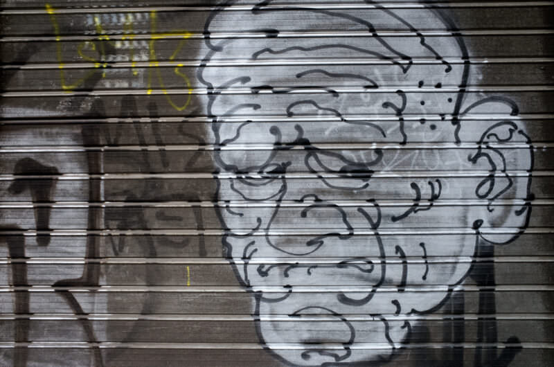 Athens graffiti on a metal shutter showing a minimalist line-drawn face in profile with flowing hair, painted in gray tones