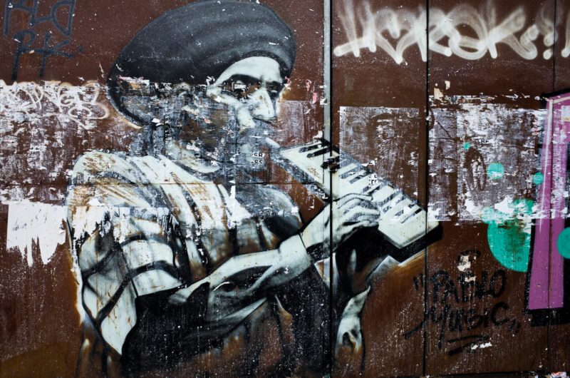 Athens stencil graffiti on a rusty metal surface depicting a bearded man in a beret holding a rifle, rendered in black and white