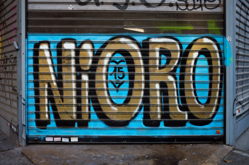 Athens graffiti on a blue shop shutter spelling "NORO" in bold gold letters with black outlines across horizontal slats