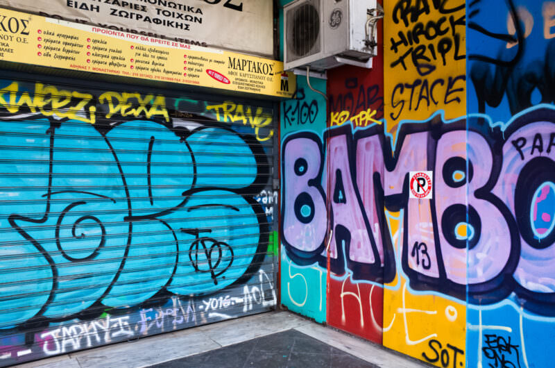 Athens graffiti on adjacent shop shutters displaying bubble-letter tags in turquoise and the word "BAMBO" in bold yellow and pink