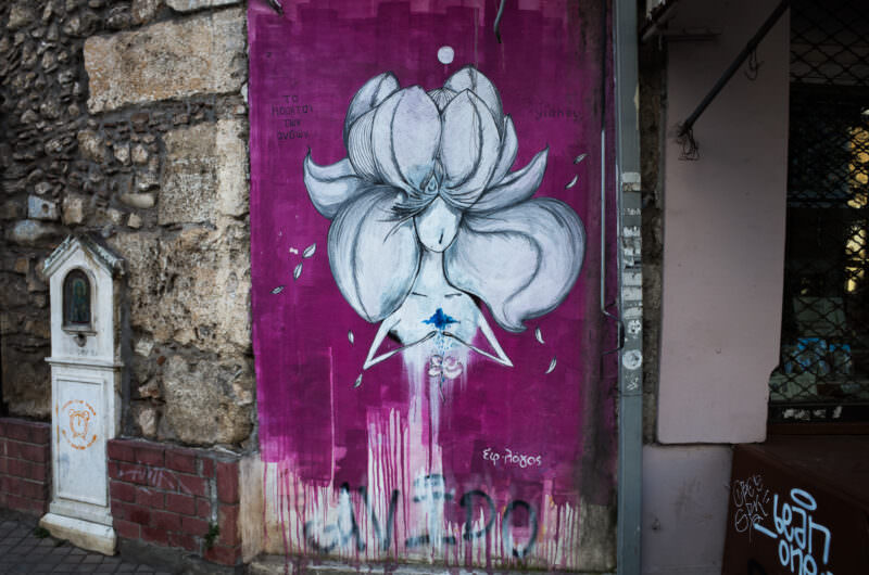 Athens street art on a door showing a white flower with dripping violet petals against a magenta background