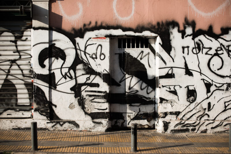 Athens graffiti wall covered in layered black-and-white abstract tags beside metal shutters and a concrete sidewalk