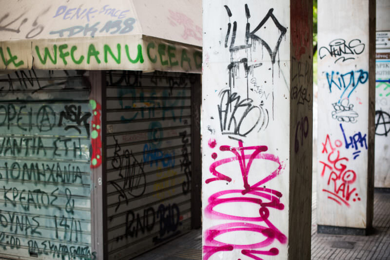 Athens graffiti tags covering concrete columns and a closed shop shutter, including handstyle lettering in black, pink, and blue