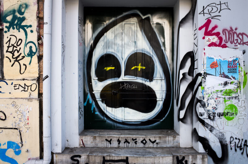 Athens street art of a cartoon dog face with large eyes and yellow-accented pupils, painted in black outlines within a doorway alcove