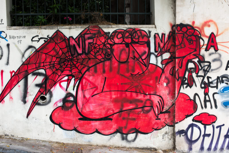 Athens street art depicting Spider-Man in a web pattern with black webbing and bold red fill, spray-painted on a white stucco wall