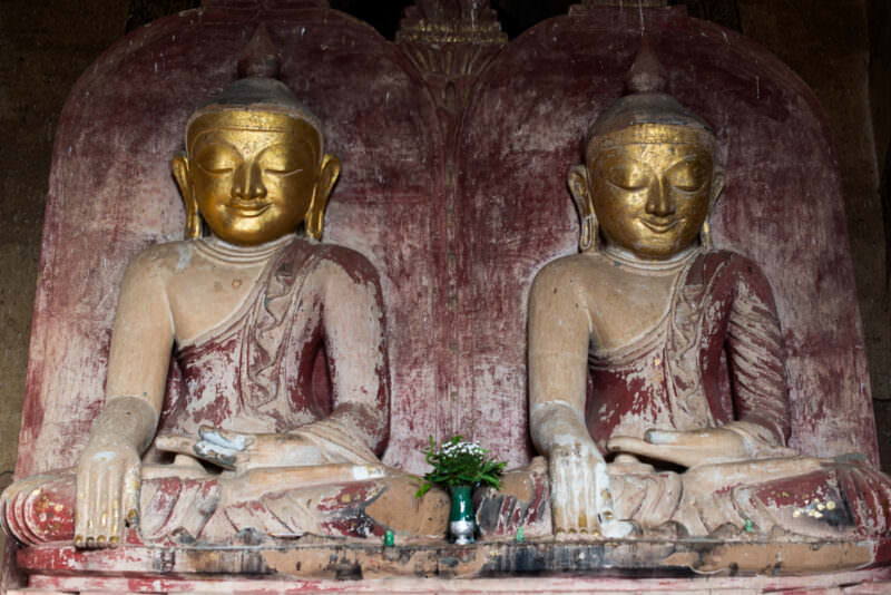 Two gilded seated Buddhas side by side in bhumisparsha mudra within Dhammayangyi Temple, their robes showing faded red pigment