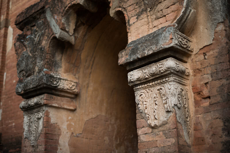 Weathered stucco capitals with foliate relief on brick archway piers at Dhammayangyi Temple, showing tightly mortared brickwork