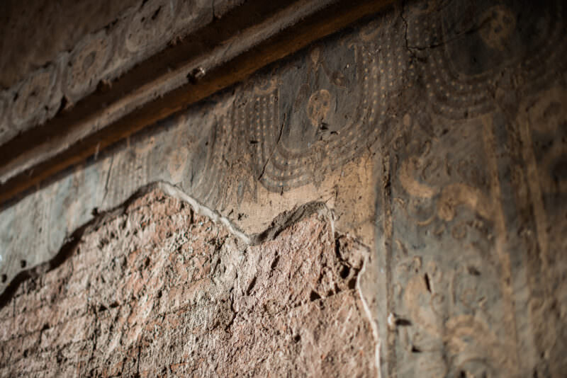 Peeling painted plaster at Dhammayangyi Temple revealing bare brick beneath, with ghost image of Buddha figure on remaining surface