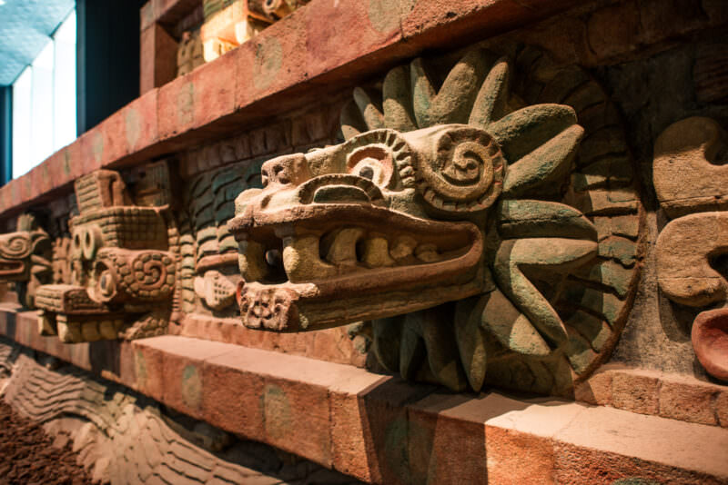 Temple of Quetzalcoatl replica facade with projecting feathered-serpent heads in ochre and green paint