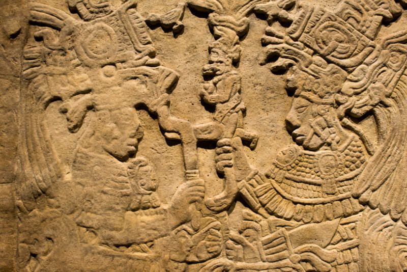 Classic Maya limestone relief panel showing elaborately costumed figures with scrollwork and standing figure between two profile heads