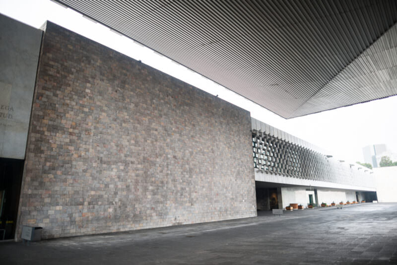Stone-clad exterior wall and aluminum celosía of museum seen from inner courtyard, geometric lattice with serpent pattern echoing Puuc ornament
