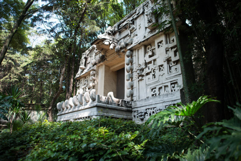Full-scale replica of Ek' Balam structure in outdoor garden, facade with stacked rounded masks and bold relief amid tropical vegetation