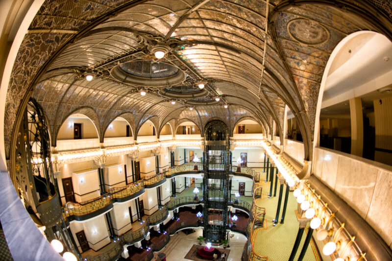 Multi-story atrium of Gran Hotel Ciudad de Mexico with curved balconies, ornate cage elevator, and vaulted stained glass ceiling