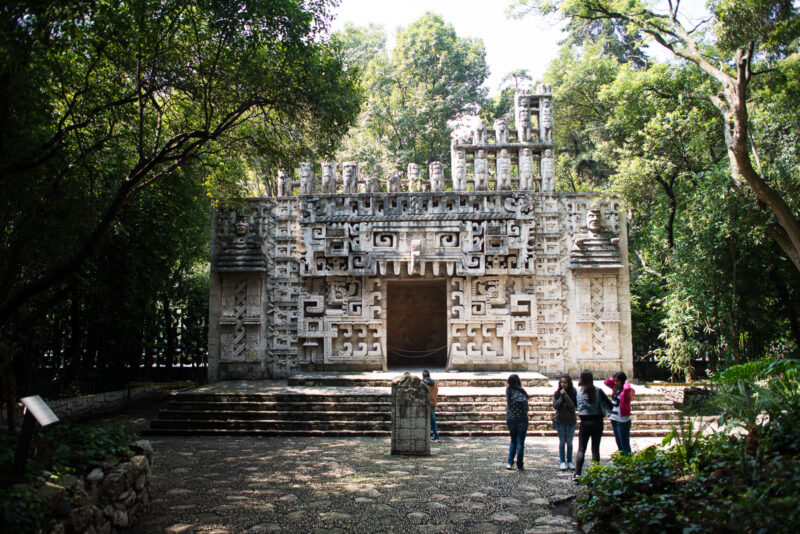 Full-scale outdoor replica of Maya palace facade covered in Puuc-style geometric mosaic stonework with roof-crest figures
