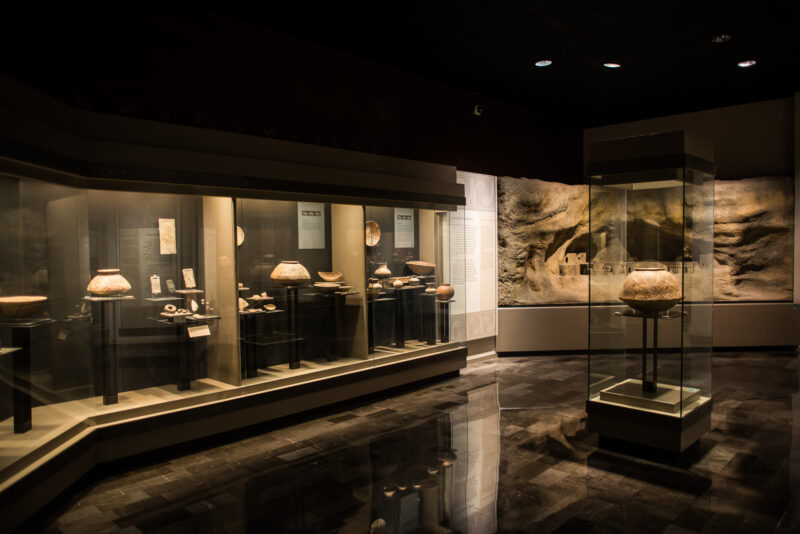 Earthenware vessels from northern Mexico in glass cases alongside diorama of cliff-dwelling settlement with rocky-cliff backdrop