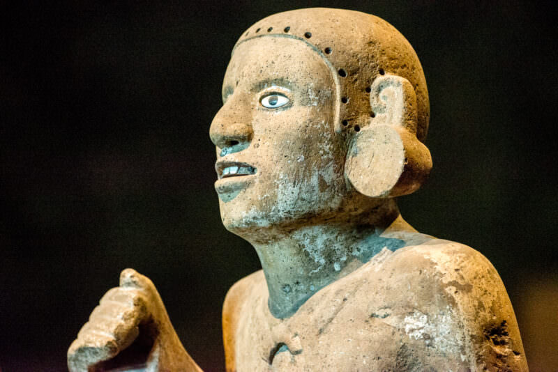 Polychrome ceramic figure in profile with upward gaze, large circular ear spool, and traces of blue-green pigment