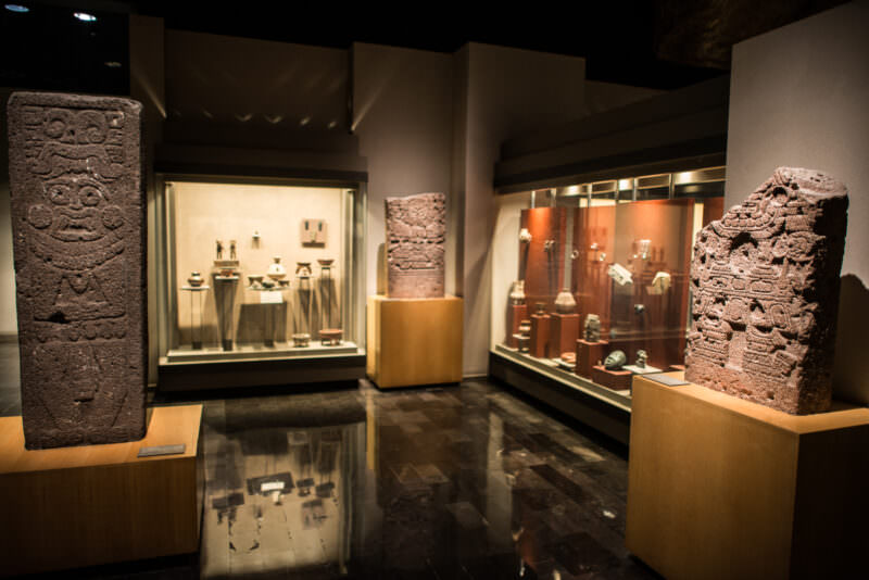 Carved dark-red volcanic stone stelae flanking display cases of smaller ceramics and ornaments in archaeology hall