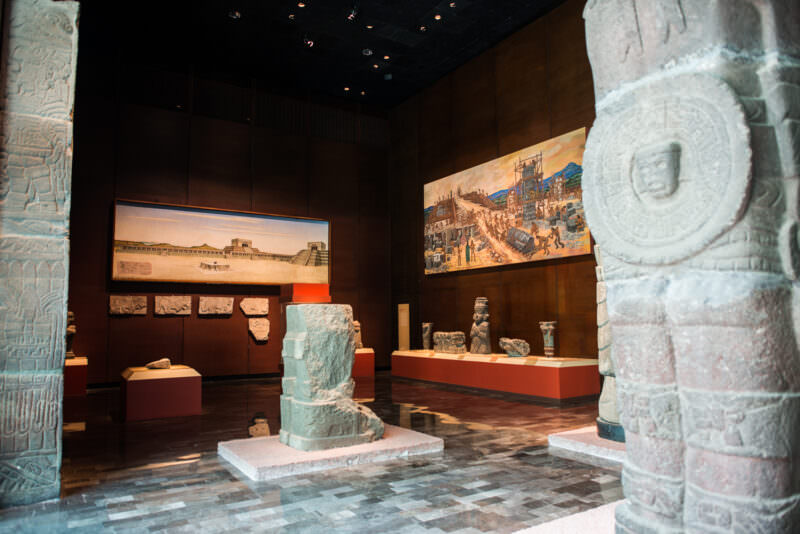 Teotihuacan hall framed by carved stone columns, reconstruction murals of the ancient city on far walls